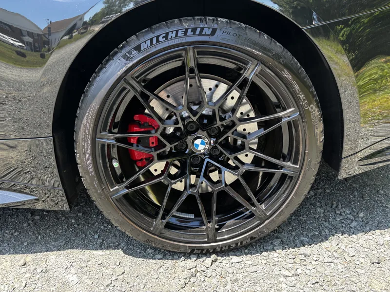 Clean black BMW alloy wheel with red brake caliper and dressed Michelin tire